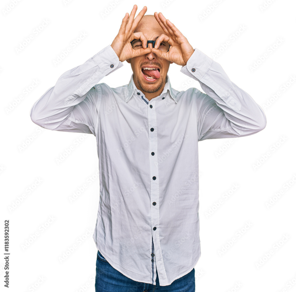 Bald man with beard wearing business shirt and glasses doing ok gesture like binoculars sticking tongue out, eyes looking through fingers. crazy expression. Bald man with beard wearing business shirt and glasses doing ok gesture like binoculars sticking tongue out, eyes looking through fingers. crazy expression.