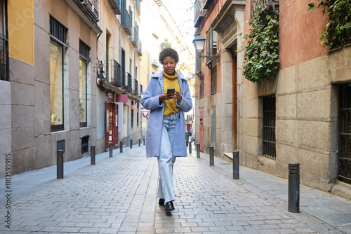 Stylish young woman using mobile phone walking in Madrid city center photo