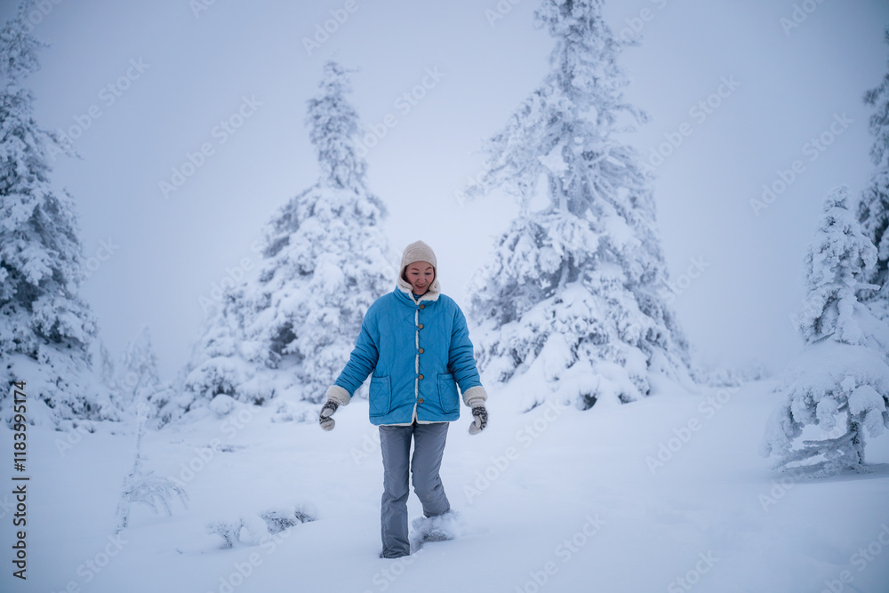 Woman in blue coat walking through deep snow in forest