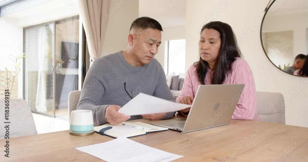 Senior asian couple reviewing documents together at home using laptop, focused and engaged Senior asian couple reviewing documents together at home using laptop, focused and engaged