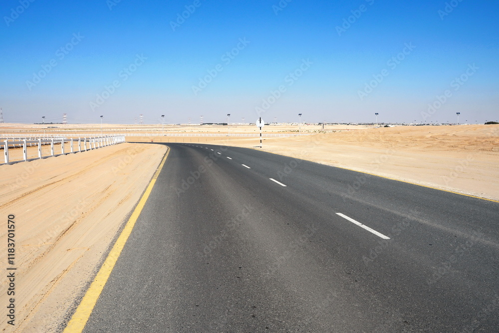Fototapeta premium Winding black asphalt road through the sand dunes of United Arab Emirates. An asphalt road zigzagging through the desert and sand dunes in the United Arab Emirates