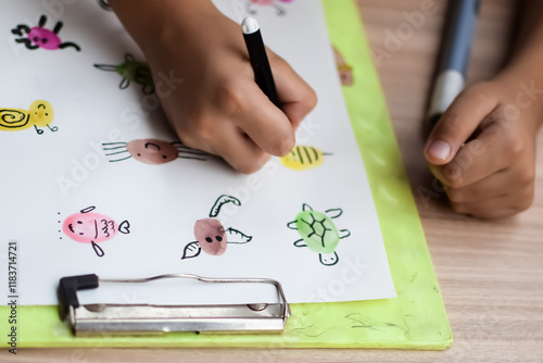Smart Indian little boy perform thumb painting with different colourful water colour kit during the summer vacations, Cute Indian Kid doing colourful thumb painting drawing on wooden table