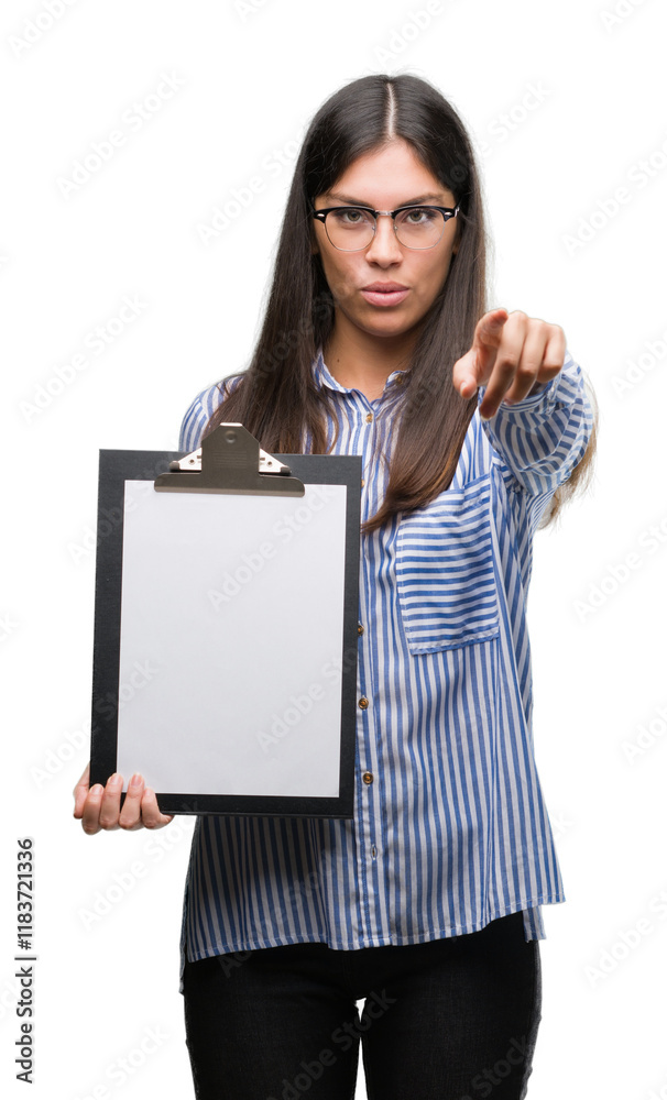 Young hispanic woman holding clipboard pointing with finger to the camera and to you, hand sign, positive and confident gesture from the front Young hispanic woman holding clipboard pointing with finger to the camera and to you, hand sign, positive and confident gesture from the front