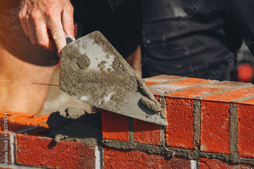 Close-up of Construction worker laying bricks with trowel during summer day at outdoor building project