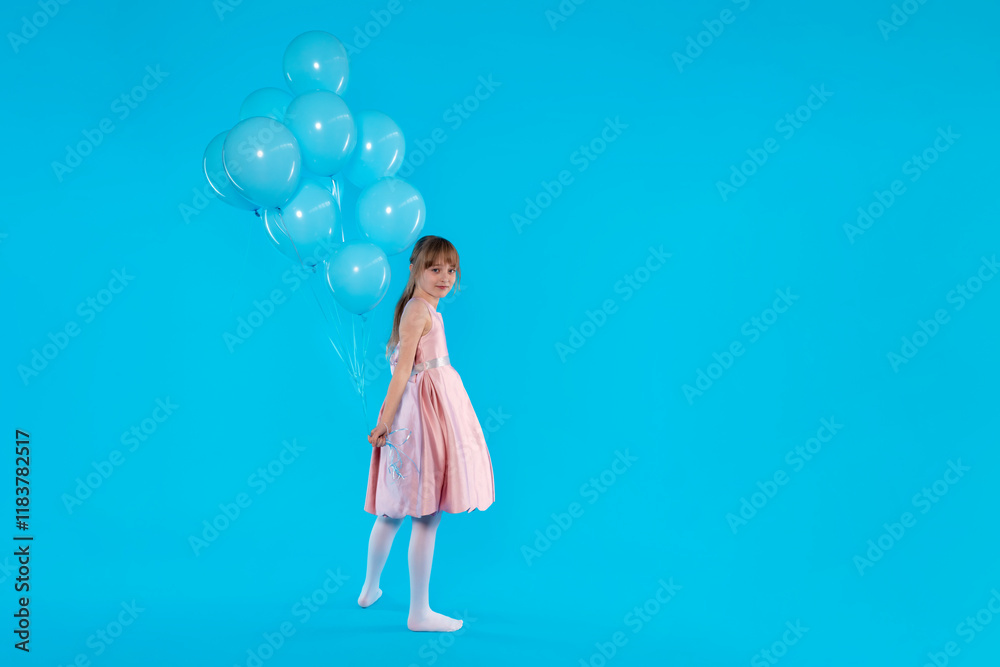 Girl in a pink dress holding blue balloons against a bright blue background Girl in a pink dress holding blue balloons against a bright blue background