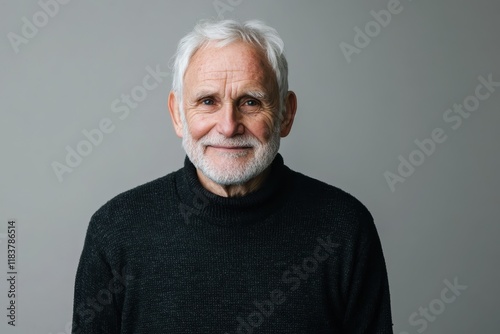 Image of an elderly man with white hair in a dark sweater gazing optimistically into the distance against a gray backdrop photo