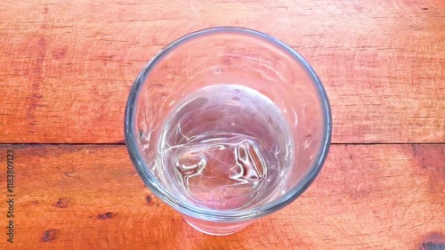 Glass of water with ice cubes on a wooden table.