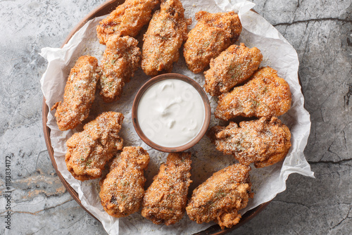 Asian fried chicken wings in cheese garlic onion breading with dipping sauce close-up in plate on table. Horizontal top view from above photo