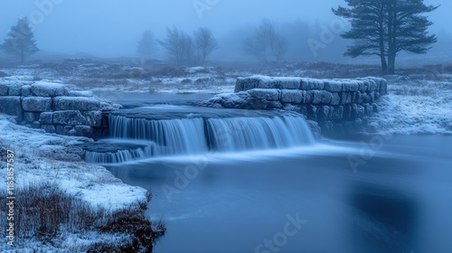 Misty winter waterfall flowing over stone weir.