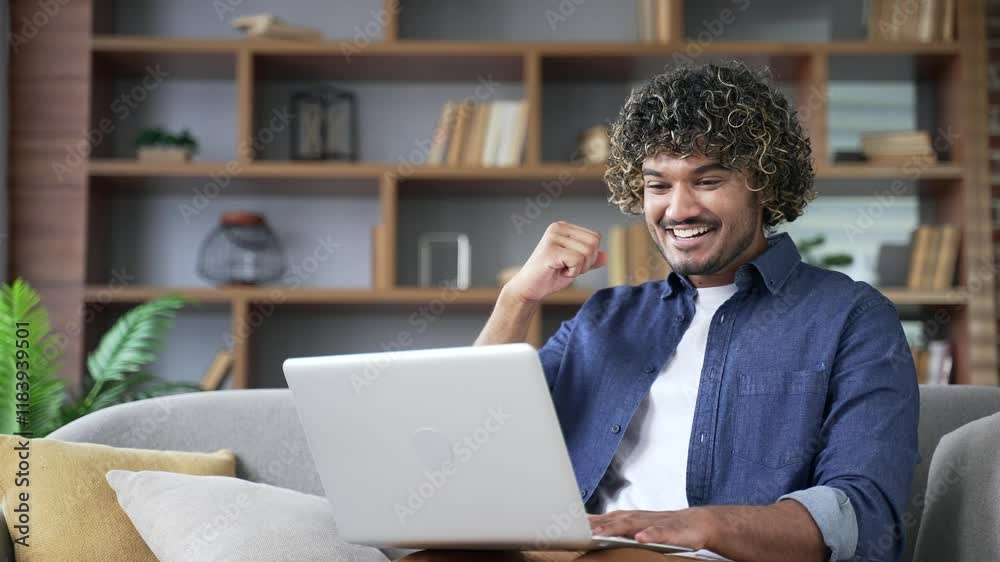 Happy excited man received great news looking at laptop screen sitting on sofa in living room at home. Smiling satisfied handsome male freelancer reads pleasant message on computer, celebrates success