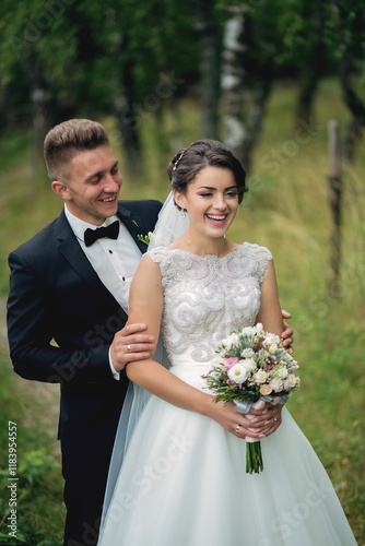 A bride and groom are posing for a picture in a field. The bride is holding a bouquet of flowers