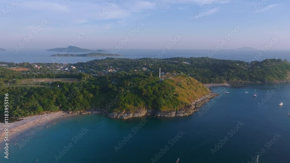 Aerial view of a green hill with a white lighthouse, lush vegetation, clear blue waters, small beaches, anchored boats, and distant islands. Aerial view of a green hill with a white lighthouse, lush vegetation, clear blue waters, small beaches, anchored boats, and distant islands.