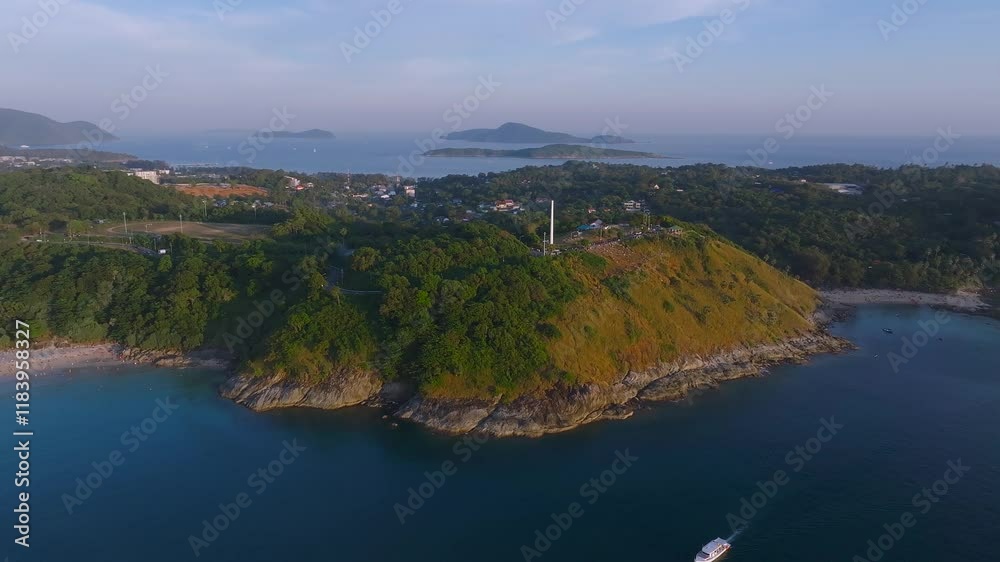 Aerial view of Phuket Island in Thailand, featuring a tall white monument on a green hill, rocky coastlines, clear waters, and distant urban areas. Aerial view of Phuket Island in Thailand, featuring a tall white monument on a green hill, rocky coastlines, clear waters, and distant urban areas.
