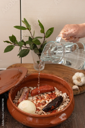 Cook pouring water into clay pot to prepare traditional Asturian fabada photo