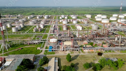 Aerial view of large industrial refinery complex with storage tanks and pipelines surrounded by green landscape