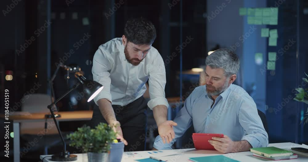 Two caucasian overworked corporate people discussing management ideas soilving financial problem using tablet computer working long hours at office.