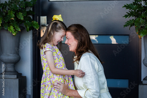 Happy mum with daughter laughing together by front door of home photo