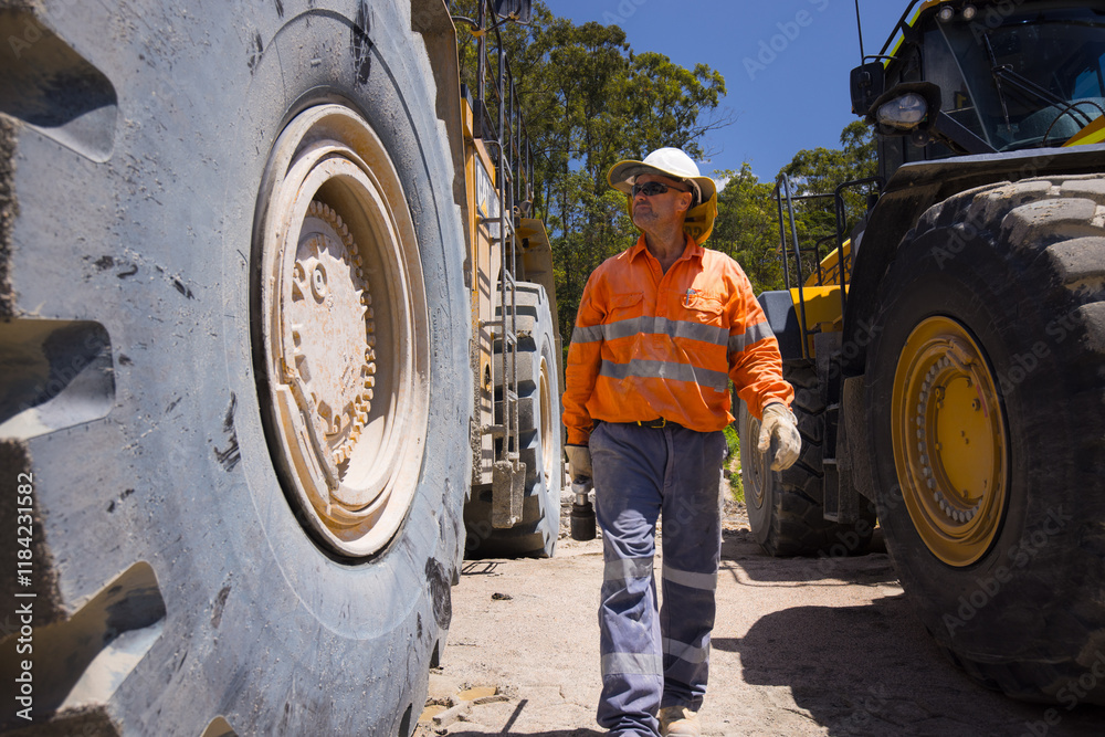Man walking in between the massive wheels of payloader dump trucks Man walking in between the massive wheels of payloader dump trucks