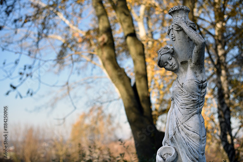 sculpture of a girl in the autumn park. An old statue in a park of a sensual semi-nude Greek or Italian Renaissance woman with a vase. sunny day, spring garden