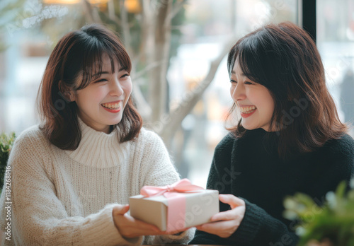 Two Japanese women exchanging gifts, one in white sweater and the other with dark hair wearing black outfit at cafe, smiling face, emotional moment, emotional scene, gift box wrapped in pink ribbon