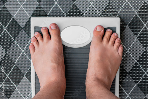 Young man measuring his weight on a bathroom scale while standing barefoot