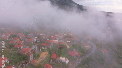 Aerial view of a tranquil village with traditional architecture and red roofs surrounded by clouds and greenery, Lagkada, Greece. photo