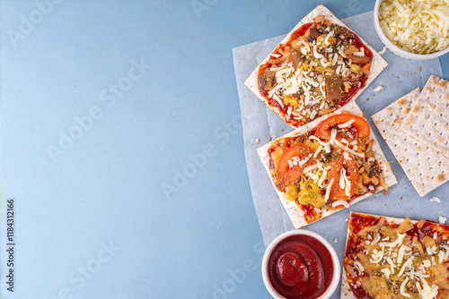 Matzah Pizza on light blue background with ingredients, cheese, tomato sauce. Food ideas and recipe for Jewish Pesach and Passover holidays photo