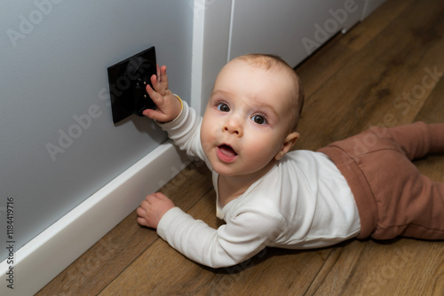 Photos A seven-month-old Caucasian baby touches a black electrical outlet on the wall