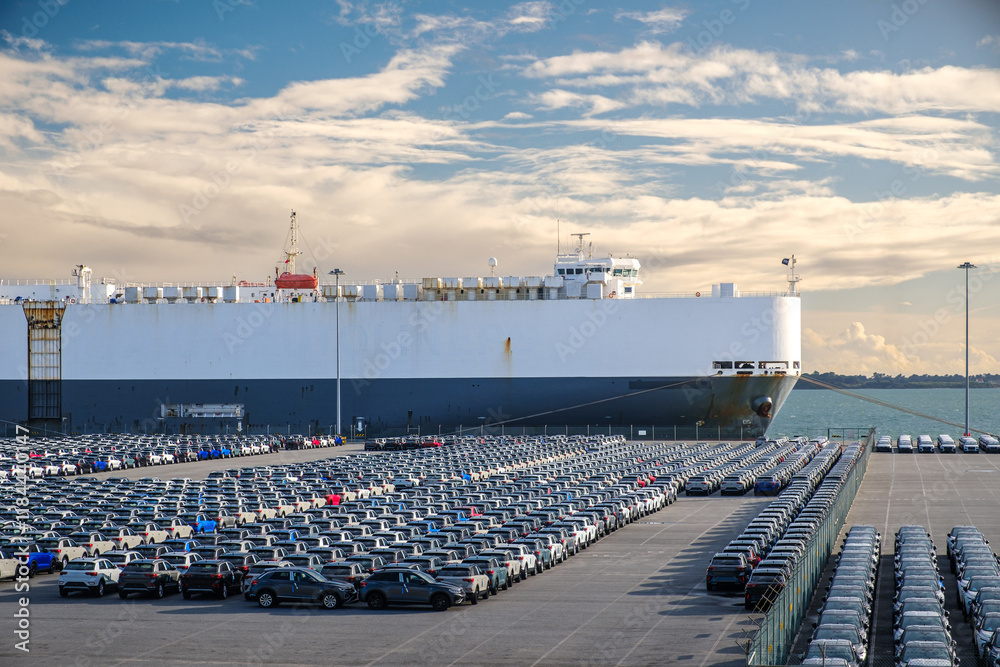 Large cargo ship docked near a vast parking lot of vehicles