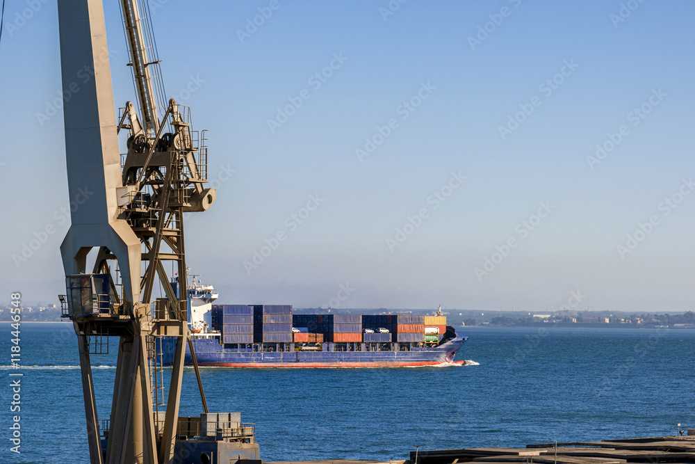 Distant container ship passing harbour and cranes fully loaded in