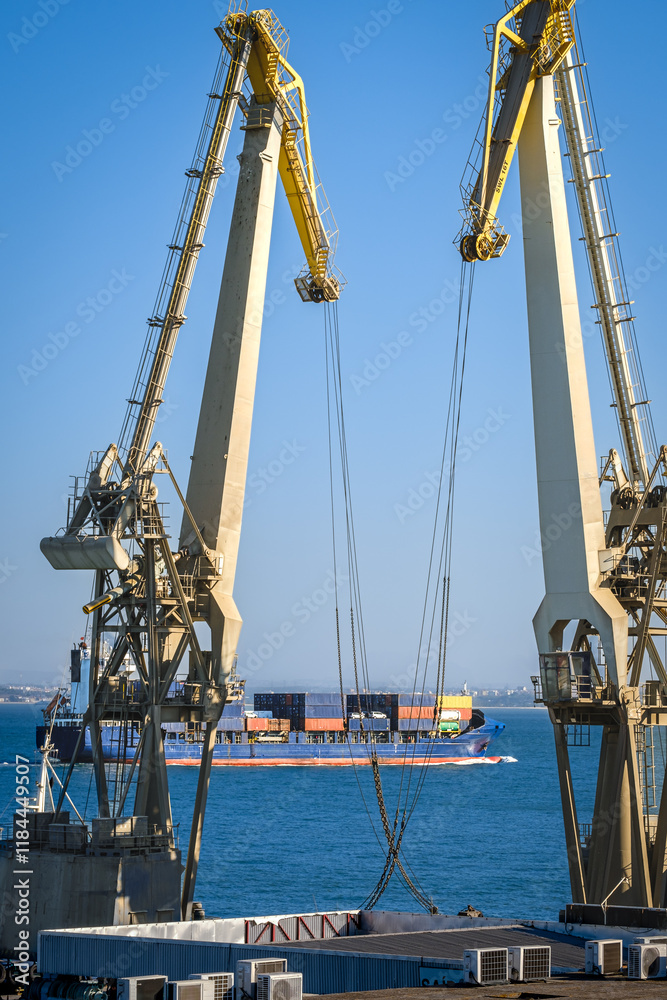 Distant container ship between two floating port cranes on a sunny day