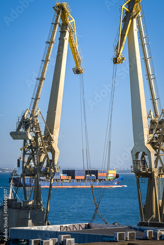 Obraz na płótnie Distant container ship between two floating port cranes on a sunny day w salonie