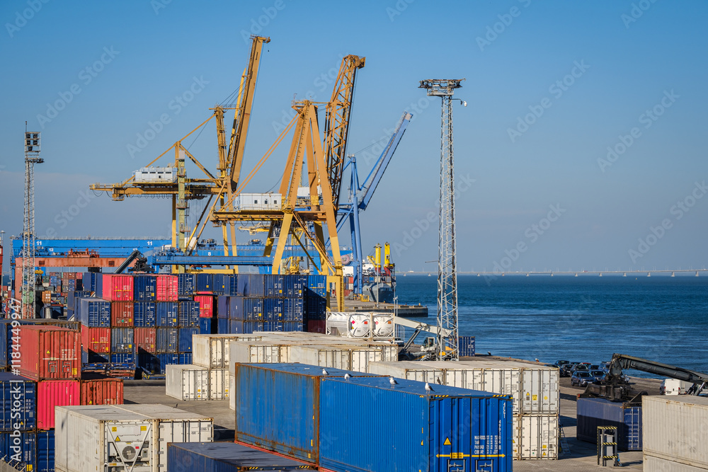 Cargo containers stacked in sea port by Ship-To-Shore cranes on sunny