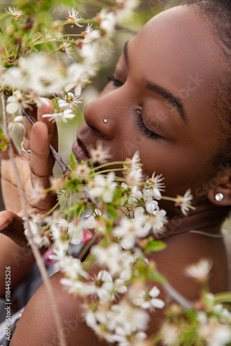 Young black woman with closed eyes smelling cherry blossoms on a tree branch in springtime, enjoying the fresh air and the beauty of nature. Meditation, mental treatment, psychology