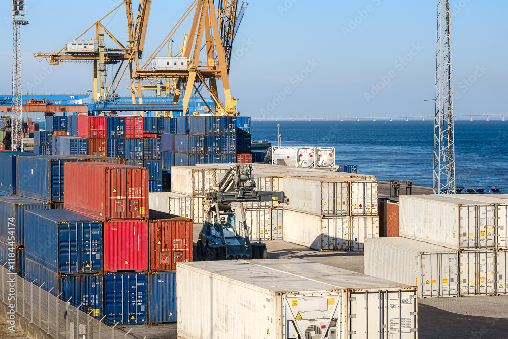 Cargo containers stacked in sea port by Ship-To-Shore cranes on sunny