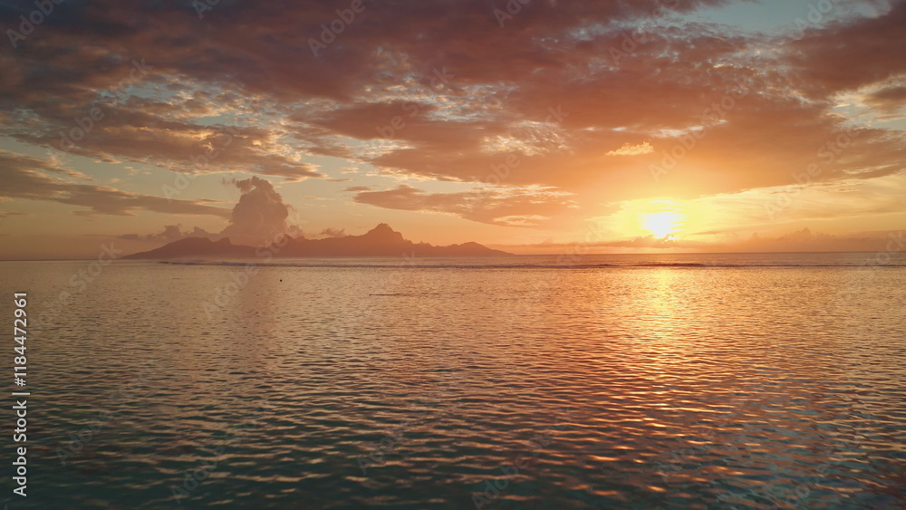 Fototapeta premium Drone fly over sunset sand beach on Tahiti tropical island. Bright orange evening sky reflects on calm ocean water waves. Beautiful sunrise landscape. Remote wild nature paradise, exotic summer travel