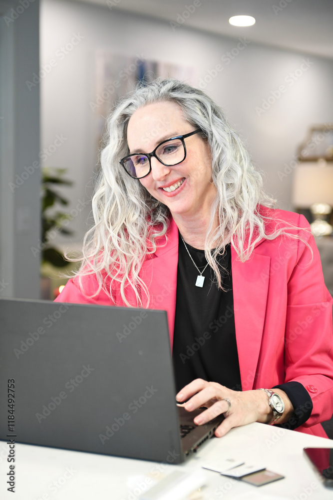 Smiling woman in pink blazer working on a laptop at a workspace. Smiling woman in pink blazer working on a laptop at a workspace.