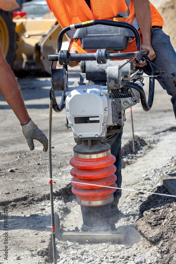 Construction workers using a compactor to prepare ground for building site in bright sunlight