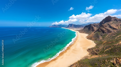 Panoramic view of a pristine beach with turquoise water, golden sand, and dramatic mountains under a vibrant blue sky.