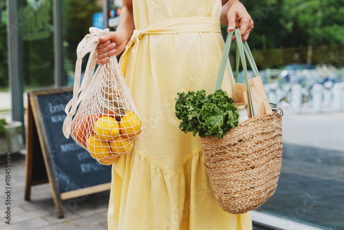 Woman holding bags with fresh organic food on storefront background of zero waste shop.