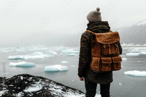 A young male with a beanie gazes at icebergs from a rocky shore, draped in mist. photo