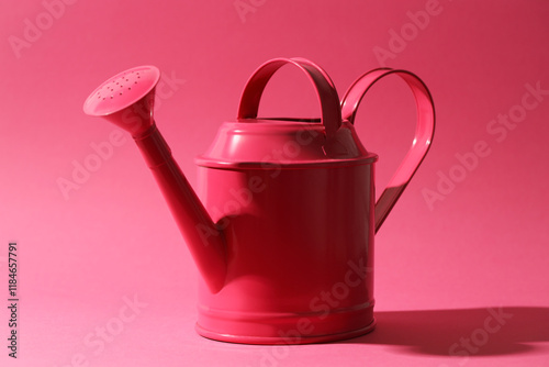 Metal watering can on bright pink background photo