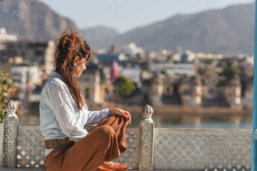 View of a serene woman sitting on a balcony with a picturesque cityscape and mountains in the background, Pushkar, Rajasthan, India. photo