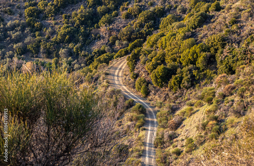 Obraz na płótnie Curved dirt road in the mountains. View from above to a waving off road route on the hills. w salonie