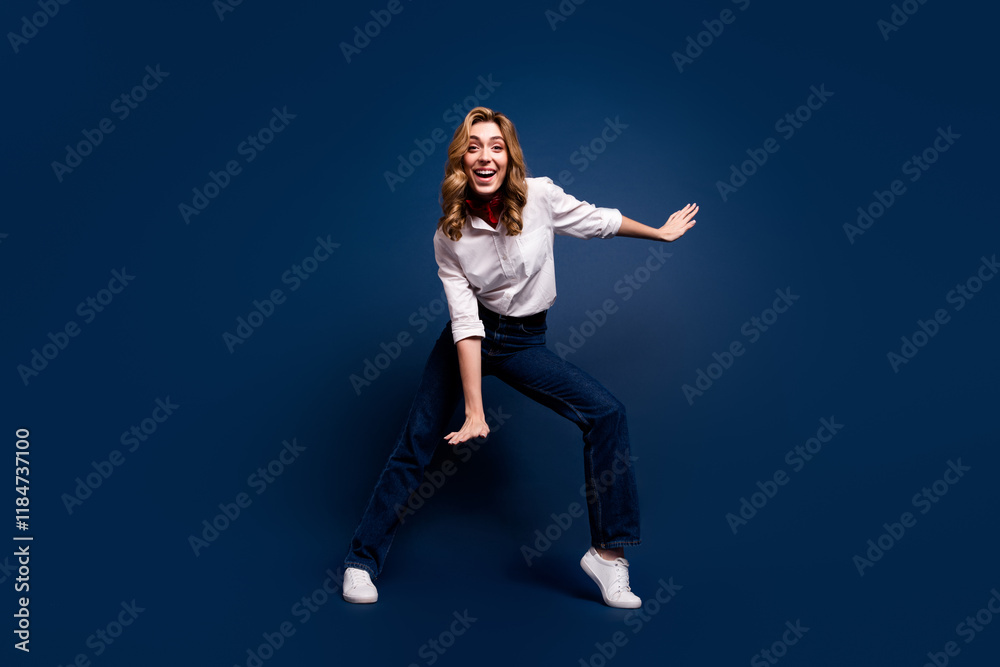 Obraz premium Joyful young woman in stylish outfit dancing against dark blue background, embracing lifestyle and fashion