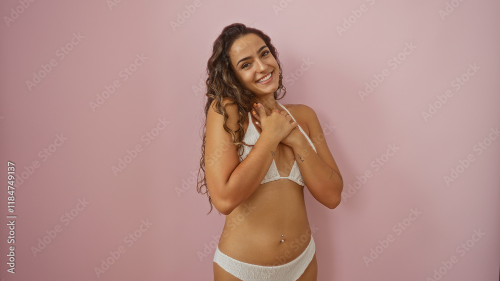 Naklejka premium Beautiful young hispanic woman in bikini posing with a smile over a pink background