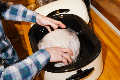 Man in plaid shirt places raw turkey in plastic bag in roaster oven