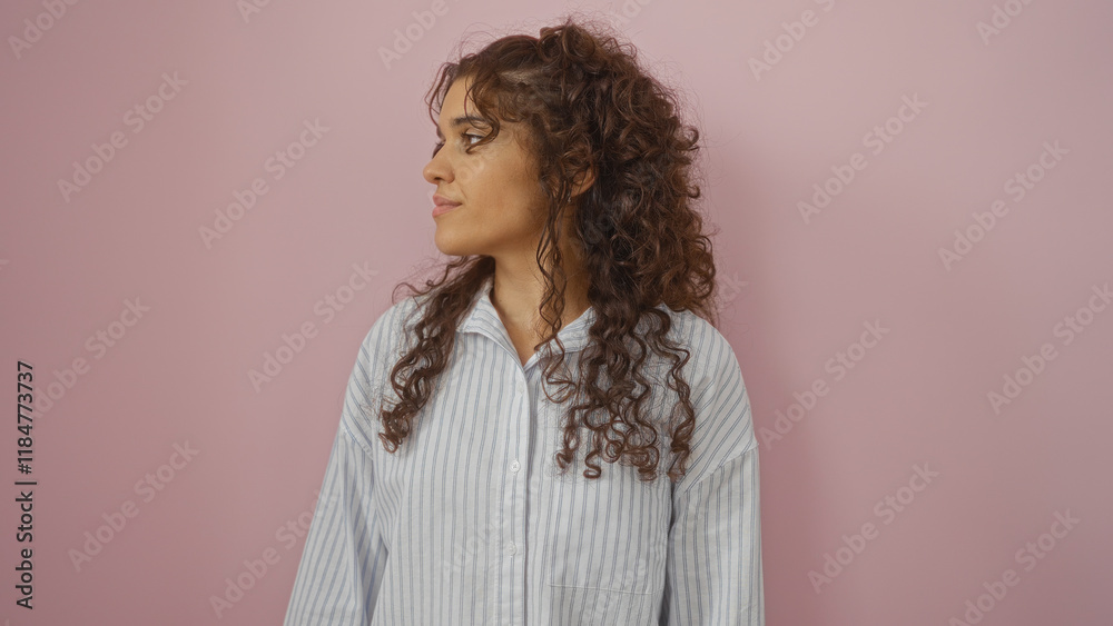 Beautiful young hispanic woman with brunette hair in a striped shirt standing over a pink background, looking to the side Beautiful young hispanic woman with brunette hair in a striped shirt standing over a pink background, looking to the side