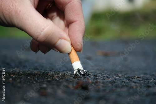 hand holding cigarette and stubs out cigarette on the ground photo