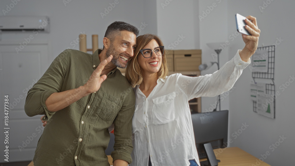 Obraz premium Employees taking a selfie during a video call in an office, smiling man and woman standing close together indoors